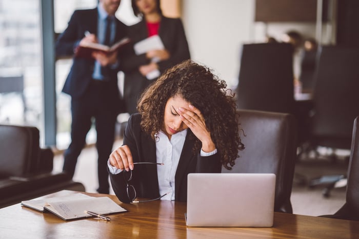 A businesswoman holds her head while sitting at a desk.