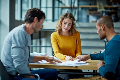 three people sitting at a table looking at documents
