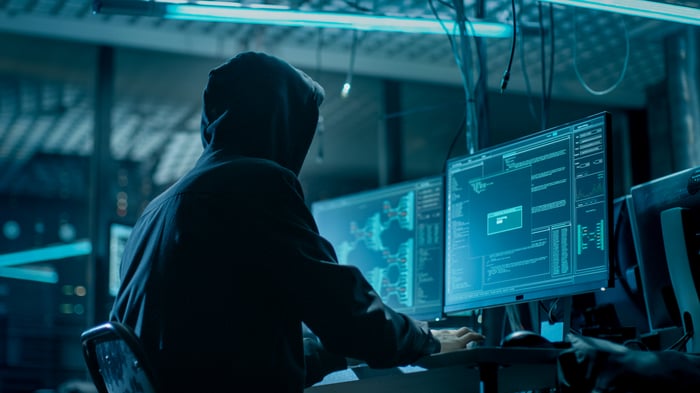 Person in hoodie at computer in dark room.