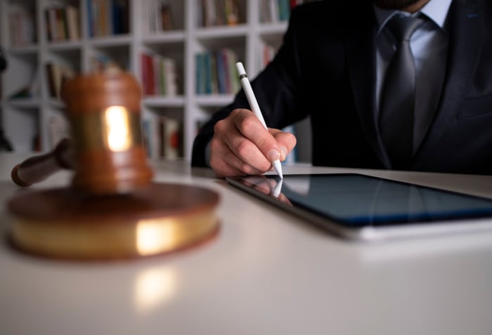 A person digitally signing a document using a tablet on a desk, beside a judge's gavel.