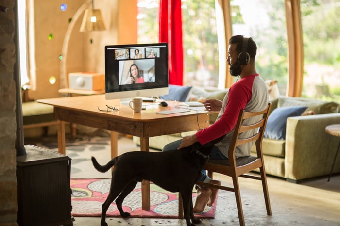 A person working from home, seated at their computer, while petting their dog.