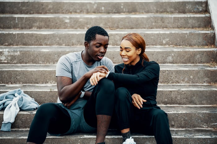 Young couple seated on steps, looking at a smart watch.