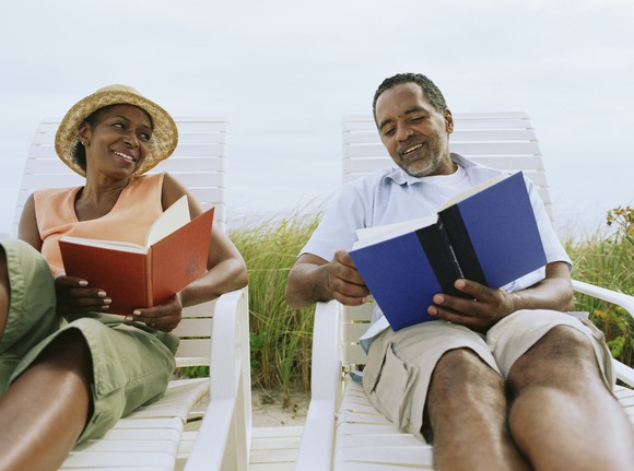 Two people outdoors reading books in lounge chairs.
