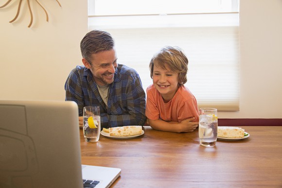 A smiling adult and child at a table with water and burritos.
