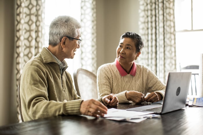 Two seniors at table with laptop and documents in front of them.