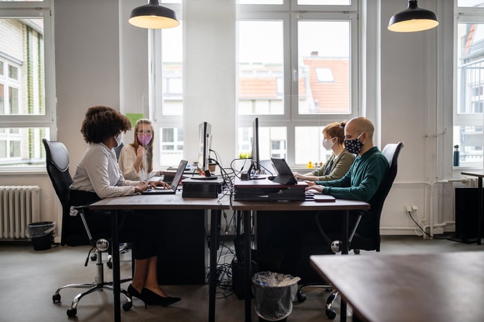 People sitting at a table with computers wearing masks.