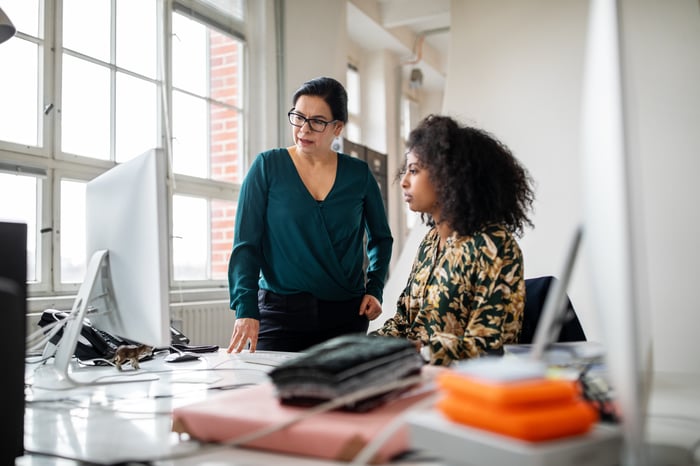 Two business women at a desk, looking at a computer monitor. 