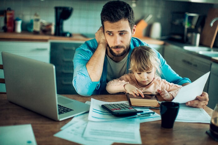 Person at table with laptop and documents holding child in lap.