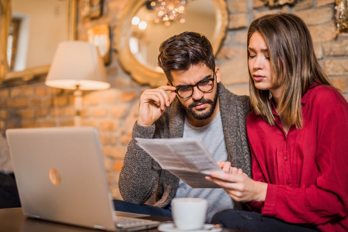 A couple looking at documents while sitting in front of a laptop.