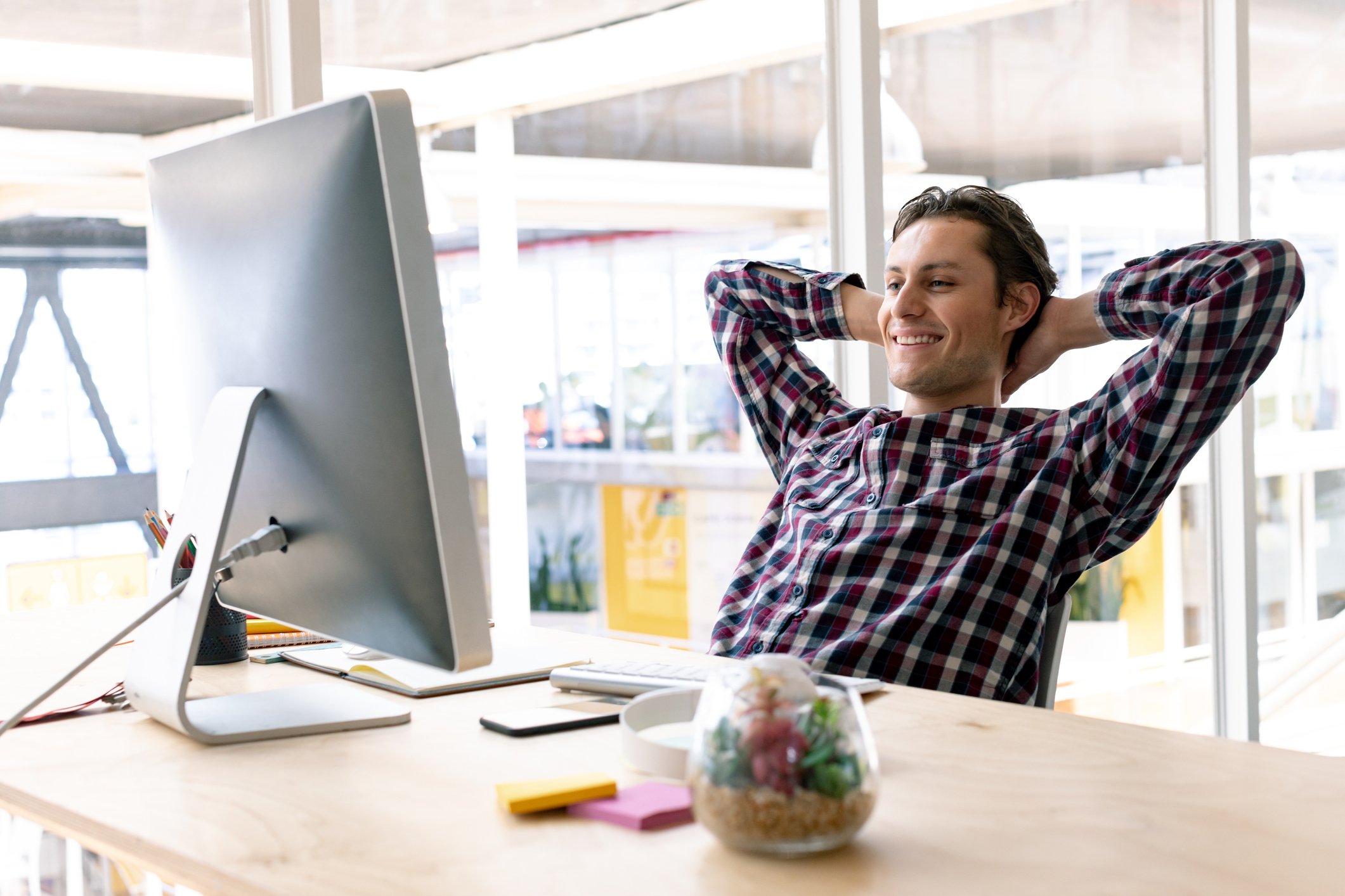 Man with hands behind his head smiling and looking at his computer monitor