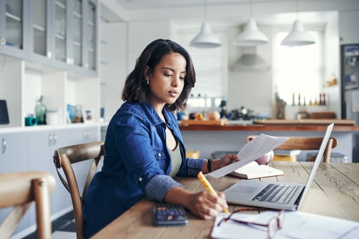 Adult works with multiple papers and a laptop in front of them at home.