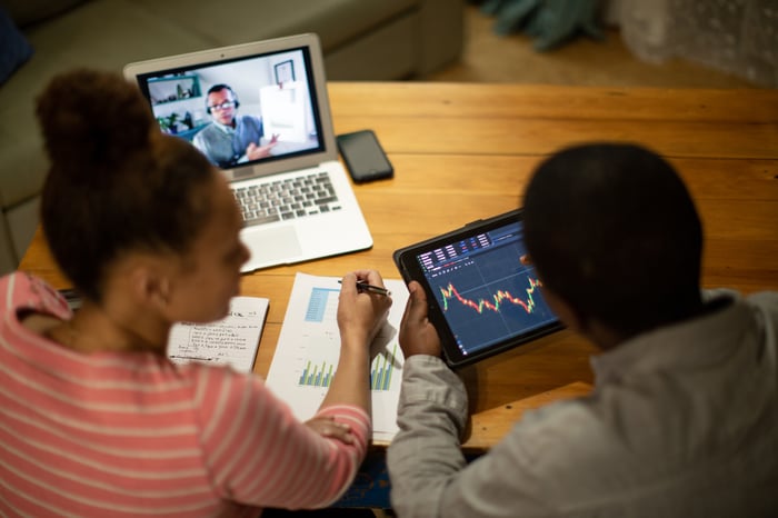 Two people at a desk conducting stock market research using charts, and watching an educational video.