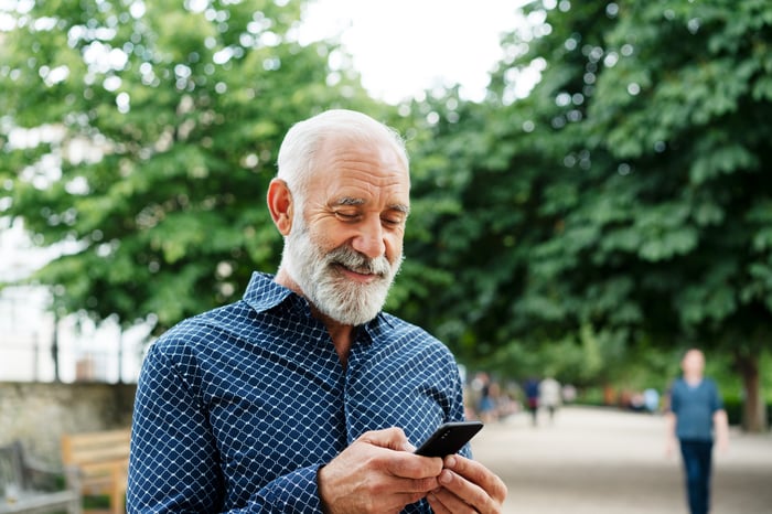 Smiling person looking at phone outdoors.