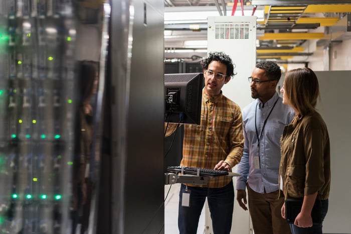 Three IT technicians looking at a computer monitor in a server room.