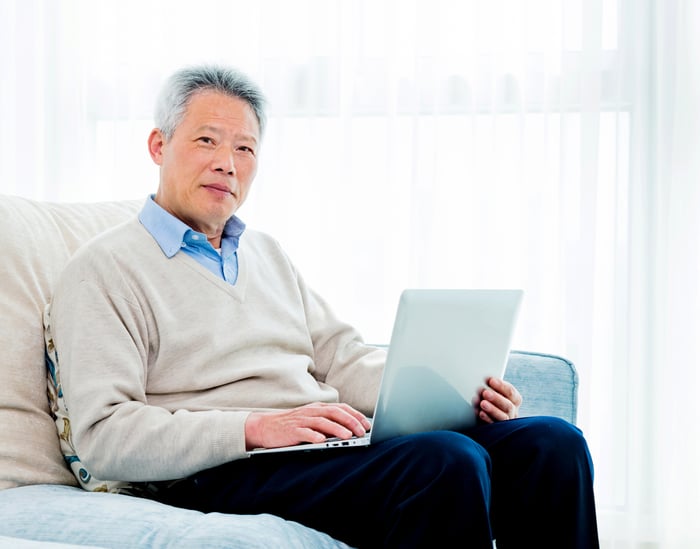 A senior working on his laptop while sitting on a couch.