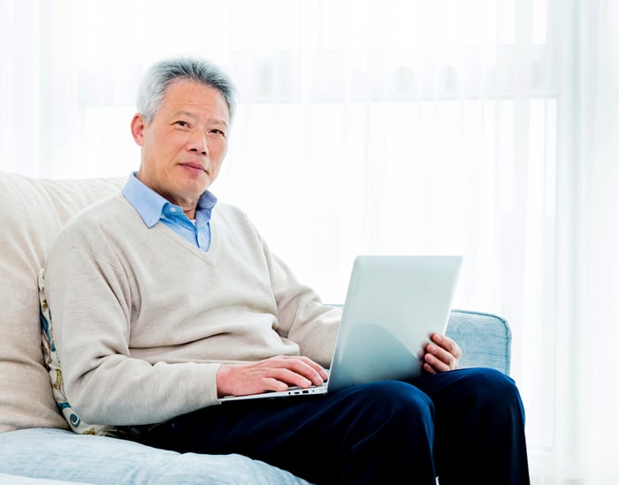 A senior working on his laptop while sitting on a couch. 