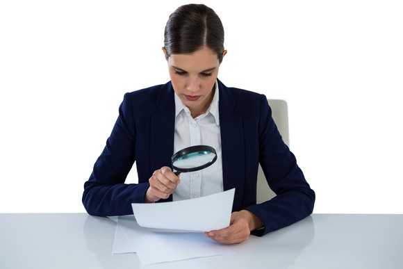 A person holding a magnifying glass over a document.