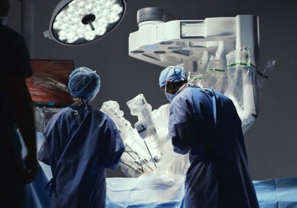 Surgeon and support staff next to a da Vinci robotic surgical system.