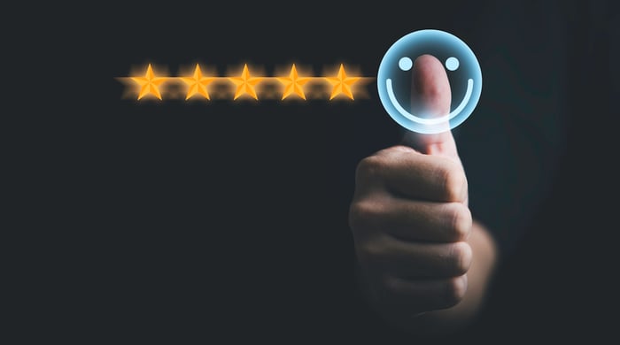 Person's thumb pushing a smiley face next to five stars on a screen.