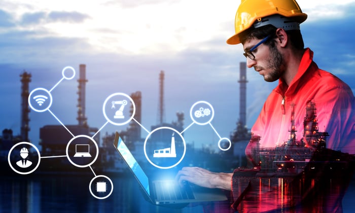 An oil rig engineer working on a laptop, with digital symbols imposed in the foreground of the photo.