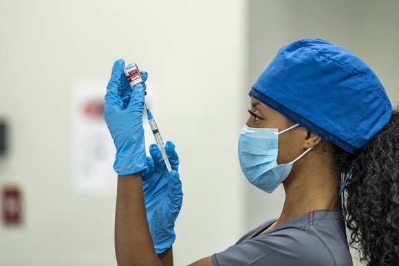 A healthcare professional holding a syringe with needle and a vaccine vial.