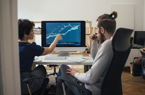 One person points to a chart on a computer, explaining the move to another person.