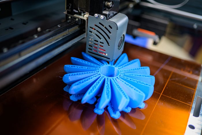 Close-up of a 3D printer producing a blue plastic fan-shaped object.