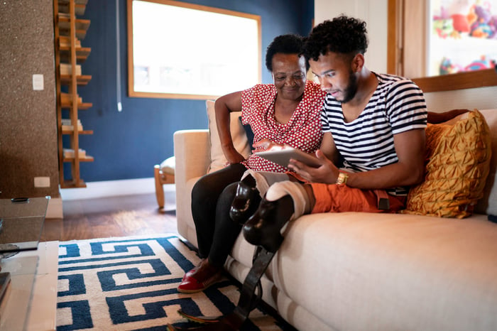 Two people sit on a couch at look at a laptop.