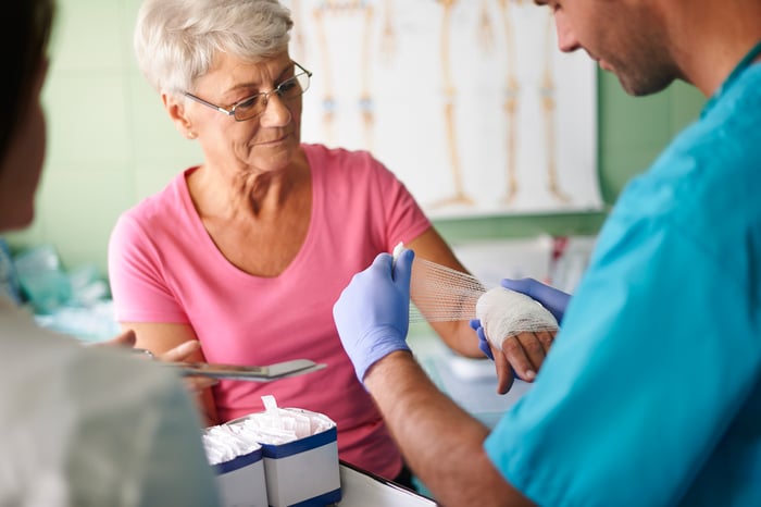 Elderly woman being treated with gauze for a wound.