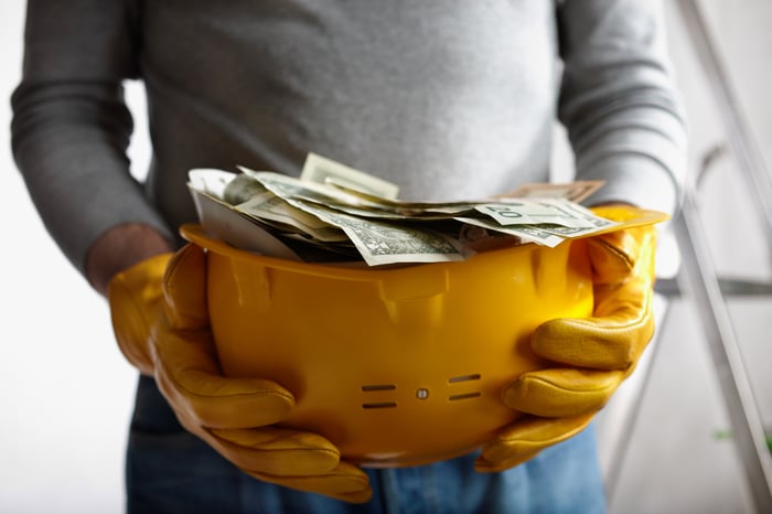 Person holding hard hat full of money.