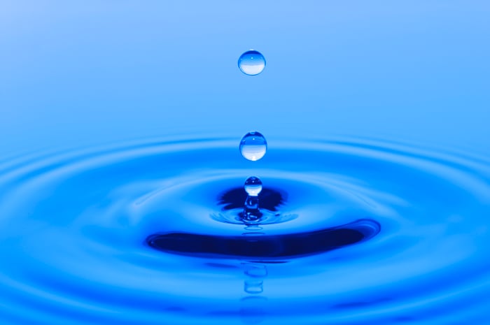 Drops of water falling into a deep blue body of water and causing ripples. 