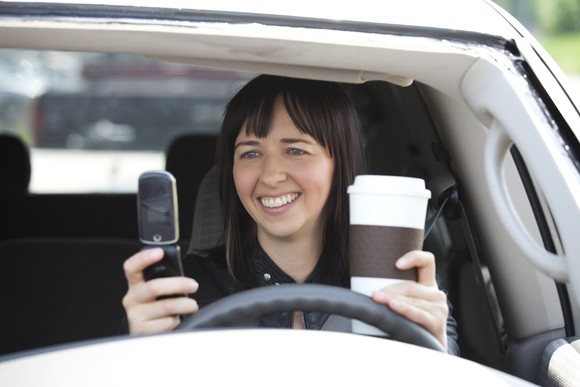 Person in car looking at phone and drinking coffee.
