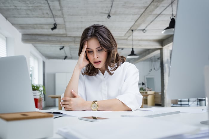 An unhappy woman holds her head while sitting at a desk.