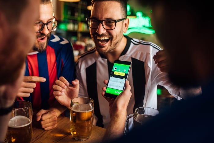 A group of friends at a bar laughing and drinking beer, looking at the sports score.