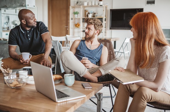 3 people talking in living room around a laptop.
