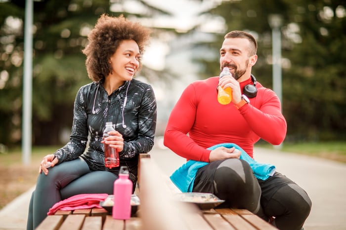 two people sitting on park bench drinking sports beverages and smiling