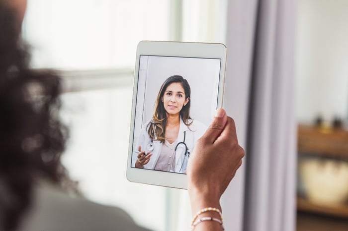 Person holding a tablet speaking to a doctor through telehealth software