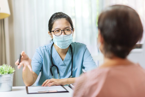 Masked healthcare professional reviewing paperwork with a patient.