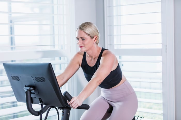 A person exercises on a bike in a bright white room.