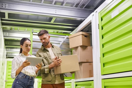 People looking at a tablet while putting stuff in a self-storage unit.