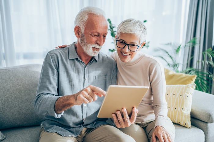 Two people sitting on a sofa while looking at a tablet.