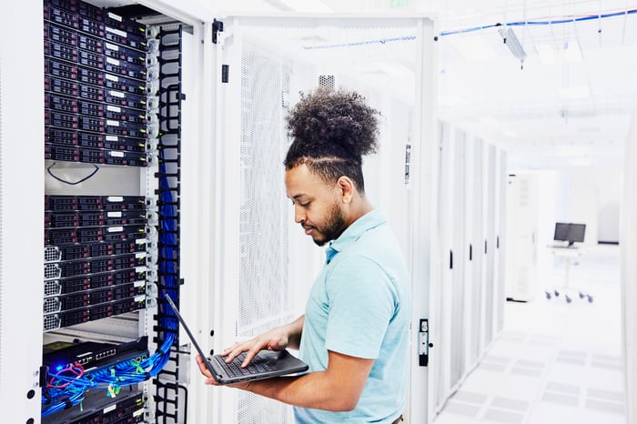 An IT professional analyzing a laptop that's plugged into a server.