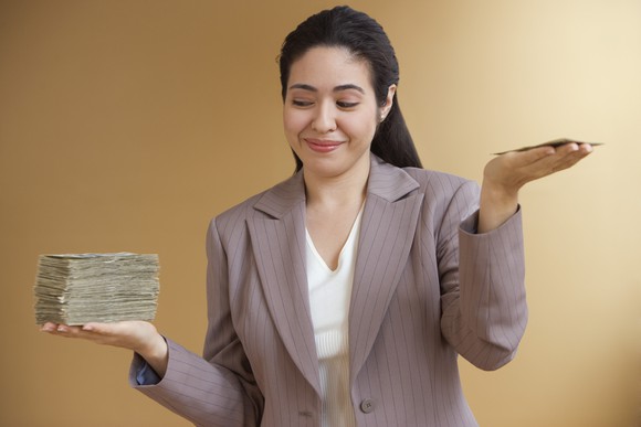 A person holding a big stack of money in one hand and a small stack in the other.