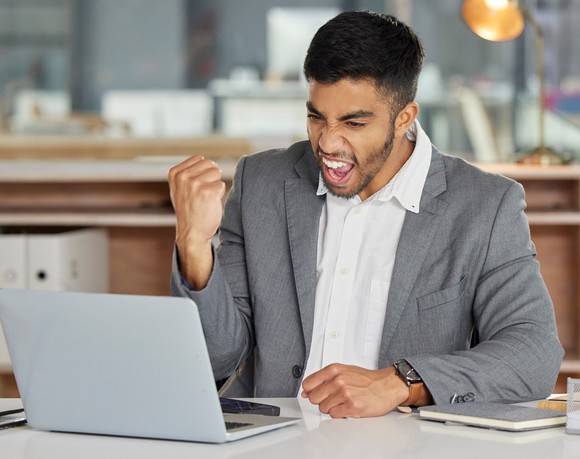 Smiling person at laptop making celebratory fist.