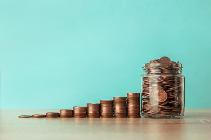 Rising stacks of copper pennies next to a jar filled of copper pennies.