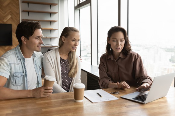 Three people looking at laptop in office.