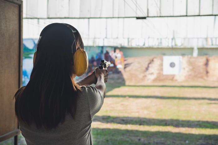 A person with a handgun at an outdoor shooting range takes aim at a target.