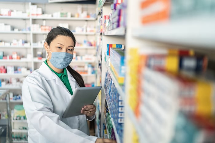 Pharmacist with tablet standing among shelves of medications.