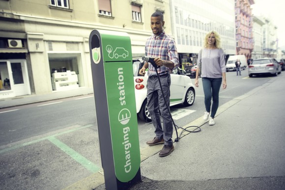 A person holding an electric car charging nozzle on the road to charge a car.
