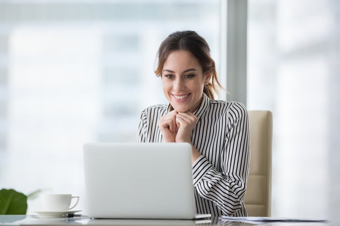 Happy smiling young woman looking at laptop screen.